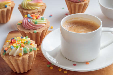 Mini cupcakes decorated with candy sprinkles and cup of coffee on white plate.の写真素材
