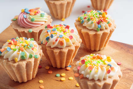 Mini cupcakes decorated with candy sprinkles on wooden background.の写真素材
