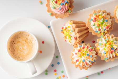 Mini cupcakes decorated with candy sprinkles and cup of coffee on white plate.の写真素材