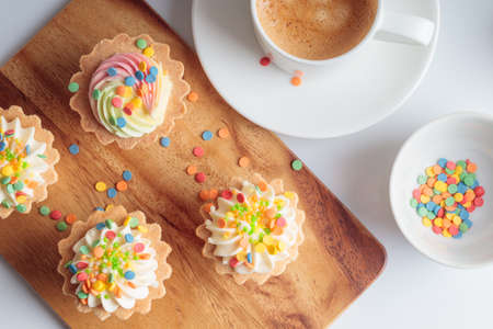 Mini cupcakes decorated with candy sprinkles and cup of coffee on wooden background.の写真素材