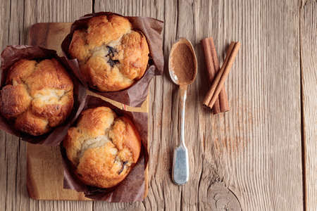 Three homemade delicious muffins and cinnamon on wooden background.の写真素材
