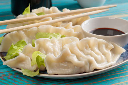 Fresh boiled Chinese dumplings with soy sauce on blue wooden background.の写真素材