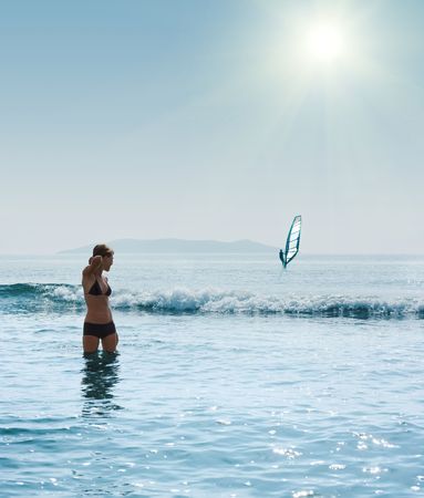 Young woman standing in blue sea and looking on windsurferの写真素材