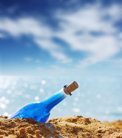 Blue glass bottle in sand and airy clouds like genieの写真素材