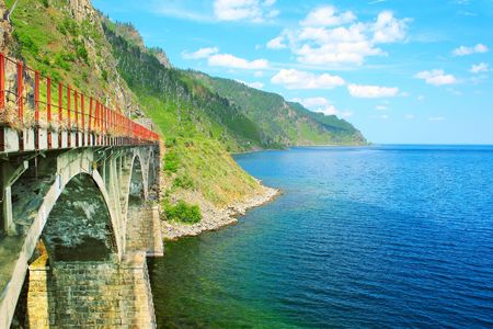 Old bridge between lake with blue clear water and mountainsの写真素材