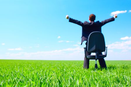 Young businessman standing on green field near chair. Focus on grassの写真素材