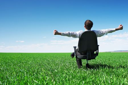 Young businessman sitting on chair in green fieldの写真素材