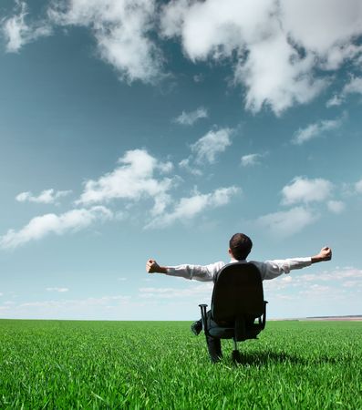 Young businessman sitting on chair in green fieldの写真素材
