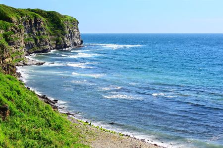 Blue sea and rocks with green grass on topの写真素材