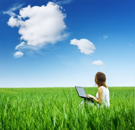 Young woman with laptop sitting on green grassの写真素材