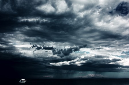 Alone white little boat on sea and dark storm cloudsの写真素材