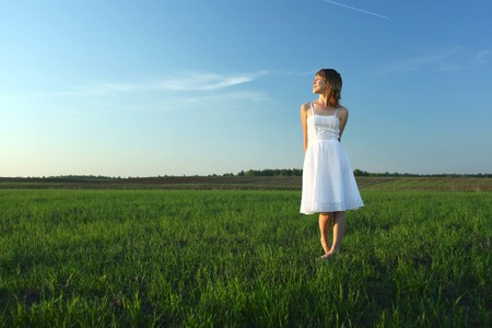 Young woman in white dress standing on meadow with green grassの写真素材