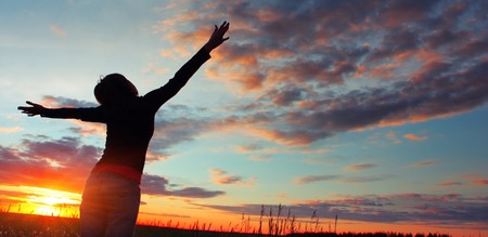 Woman standing on meadow with summer herbs over cloudy sky and sunset lightの写真素材