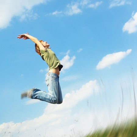 Jumping young woman over blue sky backgroundの写真素材