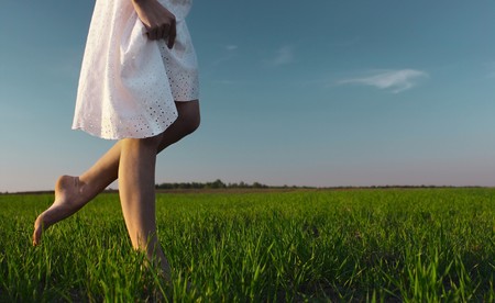 Young woman in white dress walking on meadow with green grassの写真素材