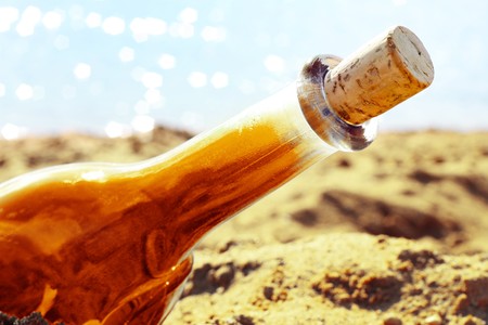 Orange bottle on yellow sand near blue waterの写真素材