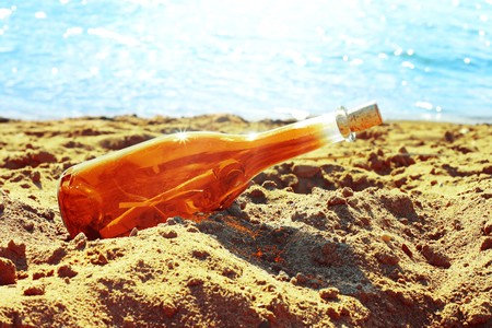 Orange bottle on yellow sand near blue water の写真素材