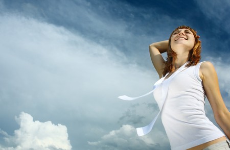Young smiling woman in white enjoing the sun over blue sky backgroundの写真素材