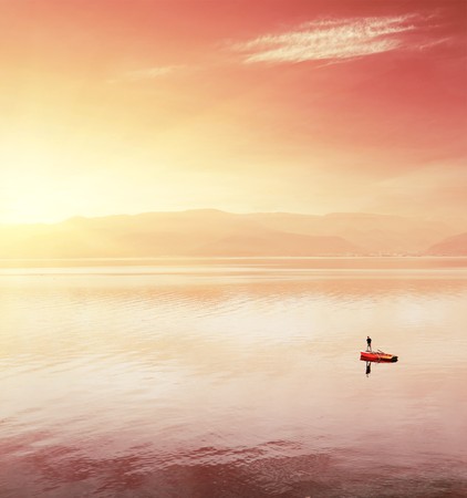 Alone fisherman in boat on huge lake under sunst lightの写真素材