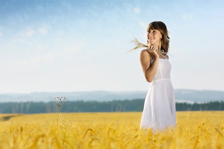 Young smiling woman in white dress standing in yellow wheat fieldの写真素材