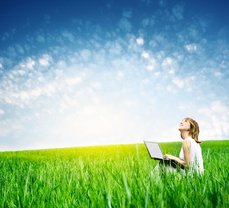 Young woman with laptop sitting on green grass and looking to a skyの写真素材