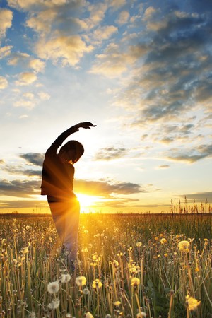 Young women doing exercises on field with grass under sunset lightの写真素材