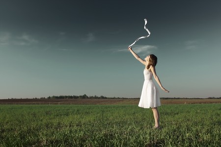 Young woman in white dress with white ribbon standing on grass over dark sky backgroundの写真素材