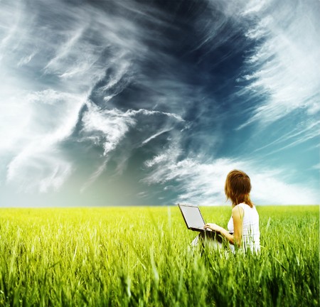 Young woman with laptop sitting on green grass and looking to the skyの写真素材