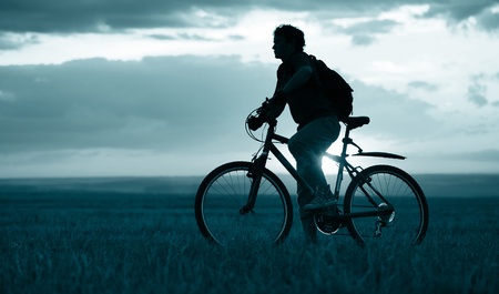 Man with bicycle standing on field on sunset backgroundの写真素材