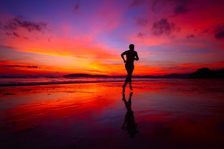 Young men jogging on wet sand by sea edge on vivid sunset backgroundの写真素材