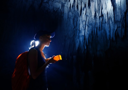 Young woman with backpack exploring cave with torchの写真素材