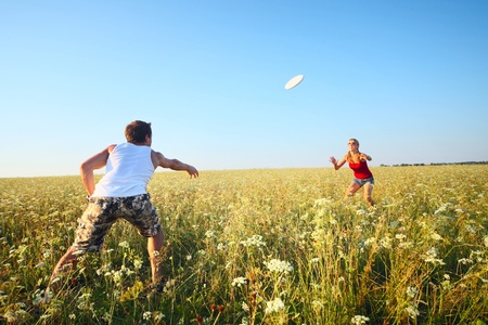 Young couple playing frisbee on a green meadow with grass on clear blue sky backgroundの写真素材