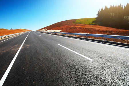 Empty countryside asphalt road through hills with red soil and clear blue sky