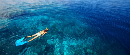 Young woman in swimsuit snorkeling in blue and transparent tropical sea