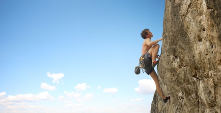 Young man climbs on a cliff over blue sky backgroundの写真素材