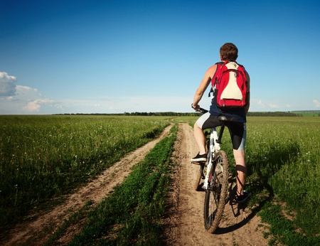 Young man standing with bycycle on an countryside roadの写真素材