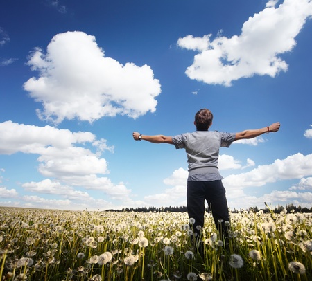 Young man with raised hands standing on a meadow with dandelionsの写真素材