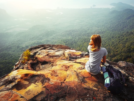 Young woman sitting on a rock with backpack and looking to the horizon