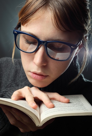 Young serious woman in glasses reading a bookの写真素材