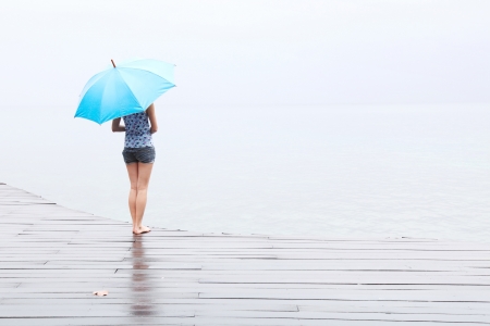 Woman with umbrella standing on a wet wooden floorの写真素材
