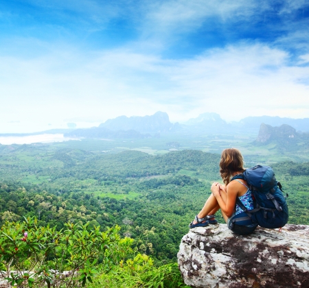 Young backpacker sitting on a cliff and looking to a valleyの写真素材