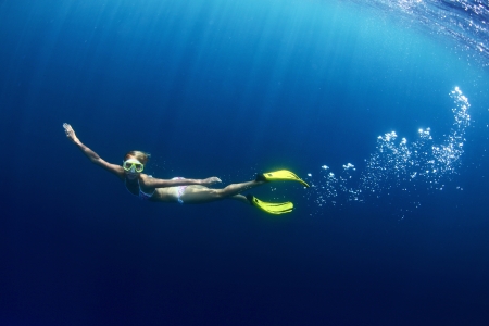 Underwater shoot of a young lady diving on a breath hold in a clear profound sea with sunbeams shining through the waterの写真素材