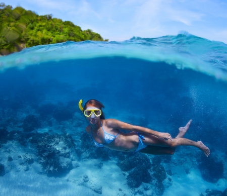 Underwater shoot of a young lady doing skin diving in tropical sea with green island on the backgroundの写真素材