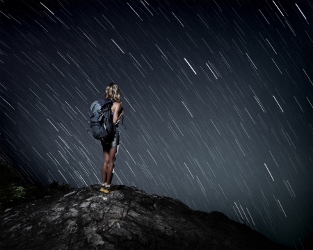 Tourist with backpack standing on top of a mountain and enjoying night sky view with starsの写真素材