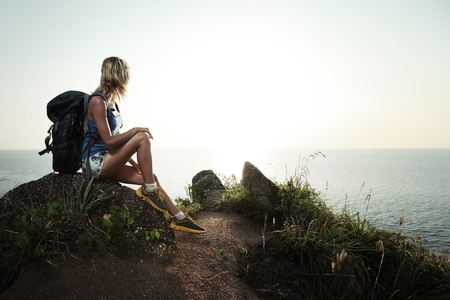 Young tourist with backpack sitting on a rock and enjoying sunsetの写真素材