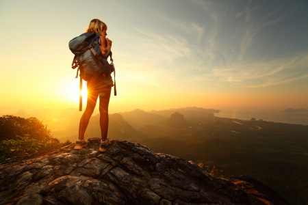 Hiker with backpack relaxing on top of a mountain and enjoying sunrise Hiker with backpack relaxing on top of a mountain and enjoying sunrise