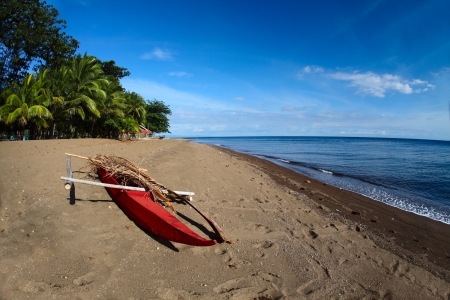 Tropical beach with dark volcanic sand and red traditional boat lying on a coast. Dauin, Philippinesの写真素材