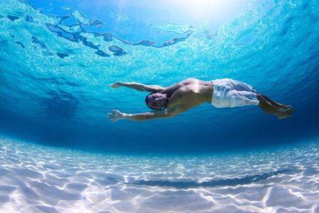 Young man diving on a breath hold in a tropical sea over sandy bottomの写真素材