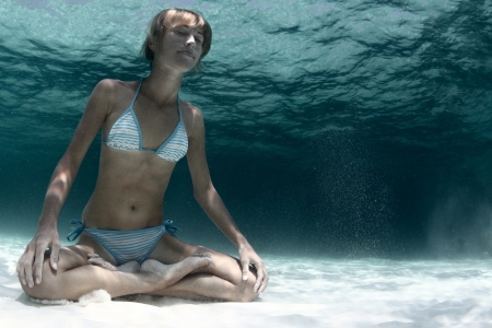 Underwater portrait of a young lady holding a breath on a sandy bottom in a yogic lotus positionの写真素材