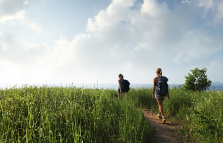 Hikers with backpacks walking through tropical lush meadowの写真素材